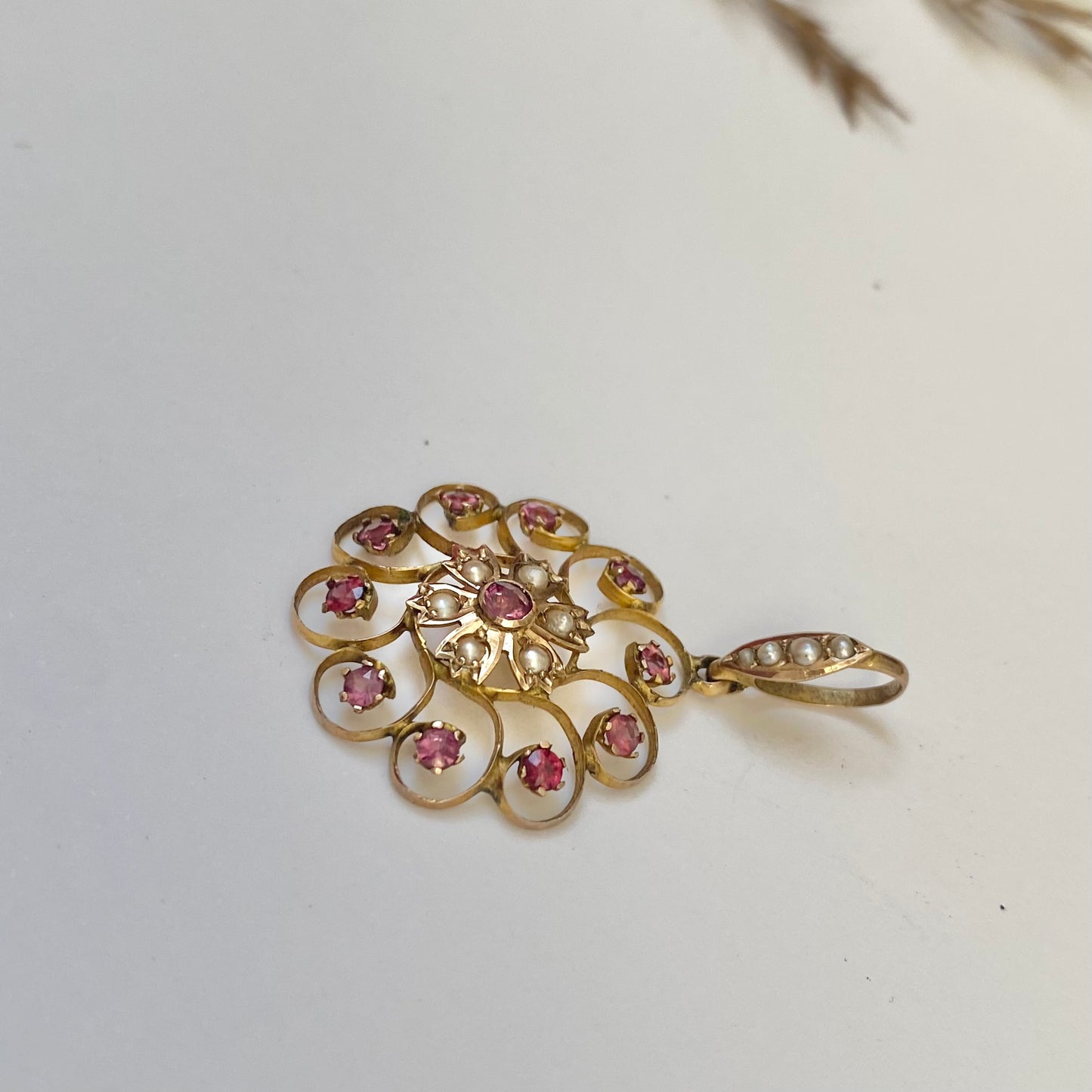 An early 20th century naturalistic 9ct gold garnet and split pearl wreath pendant.