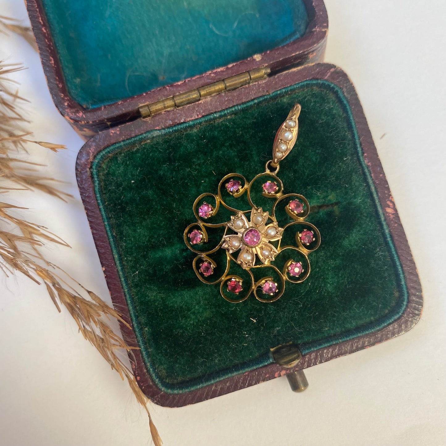An early 20th century naturalistic 9ct gold garnet and split pearl wreath pendant.
