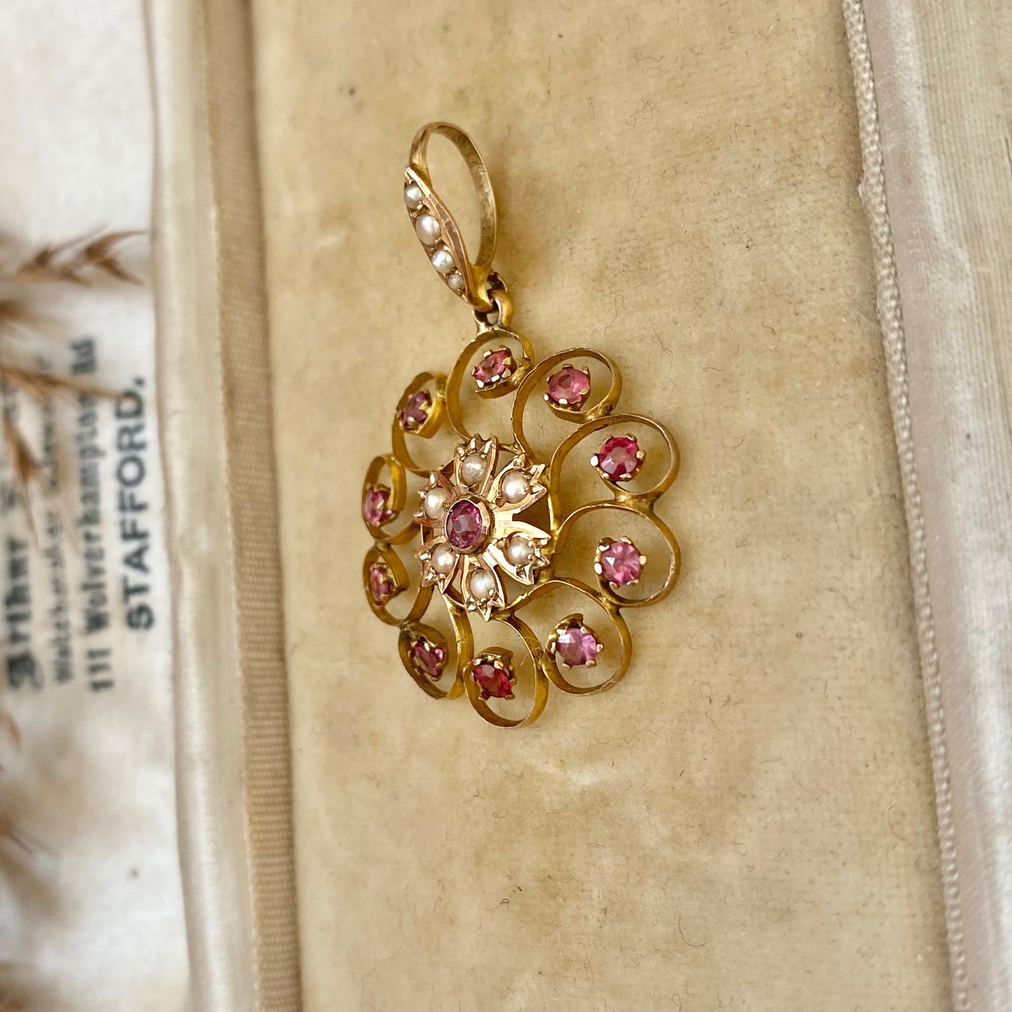 An early 20th century naturalistic 9ct gold garnet and split pearl wreath pendant.