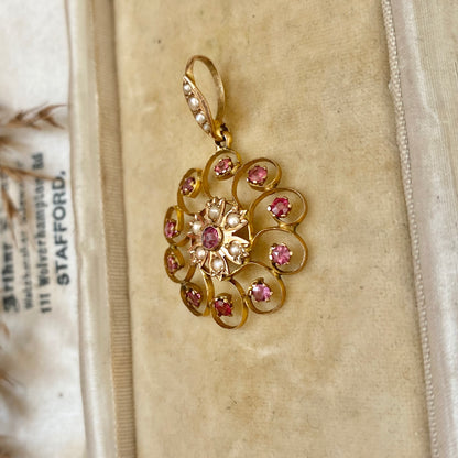 An early 20th century naturalistic 9ct gold garnet and split pearl wreath pendant.