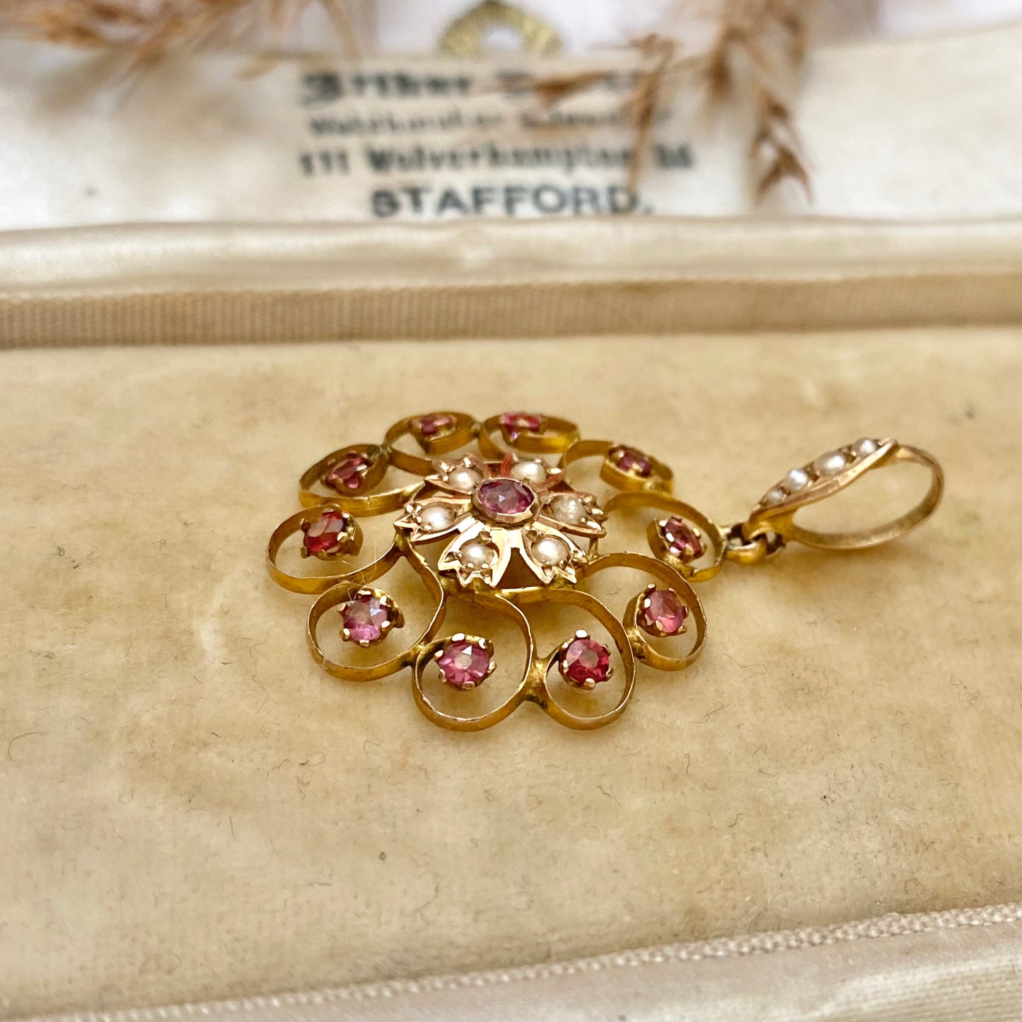 An early 20th century naturalistic 9ct gold garnet and split pearl wreath pendant.