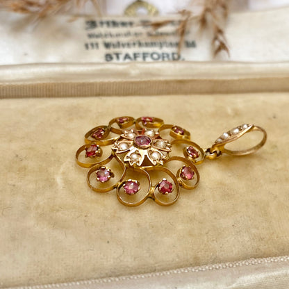 An early 20th century naturalistic 9ct gold garnet and split pearl wreath pendant.
